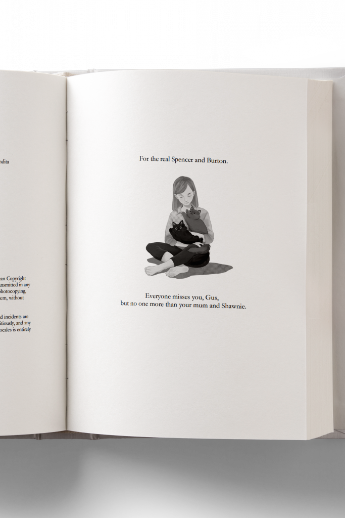 A 3D mockup of a print book interior showing the dedication page with a drawing of a young woman sitting on the floor with two cats in her arms and the words "For the real Spencer and Burton."