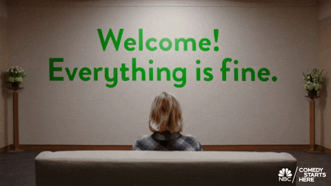 A blonde woman sitting on a couch looking at the wall that says "Welcome! Everything is fine!"