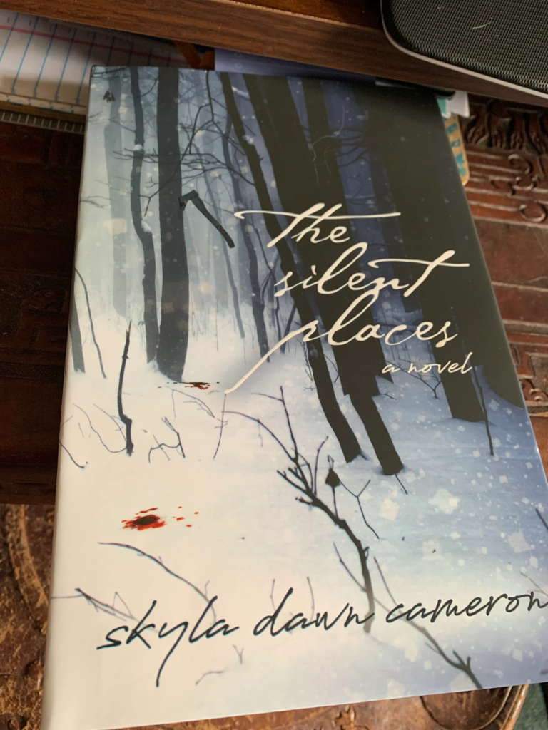 The Silent Places jacketed hardcover with an alternate cover showing a snowy forest with an axe lodged in a tree and red spots of blood.
